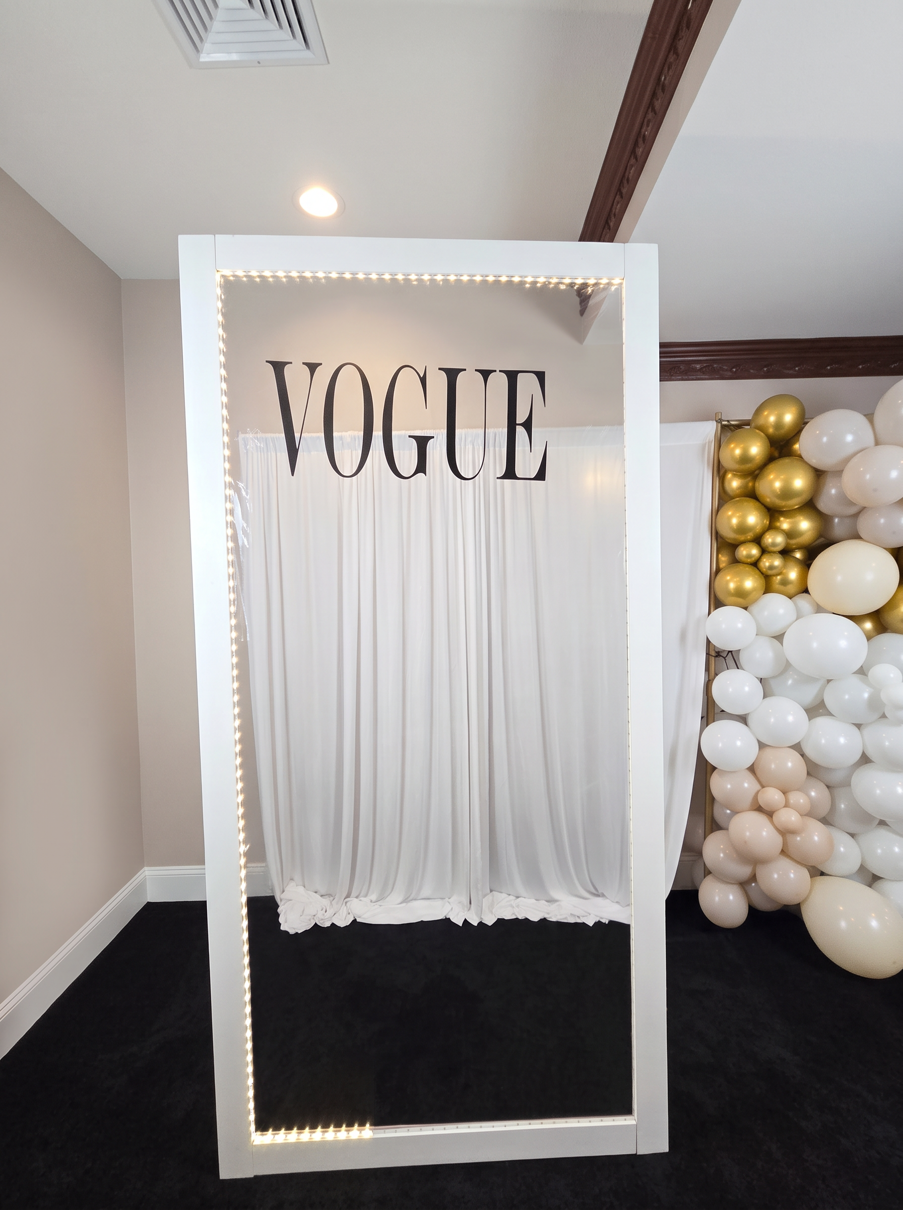 Lighted magazine cover photo frame with white draping beside a white and gold balloon garland
