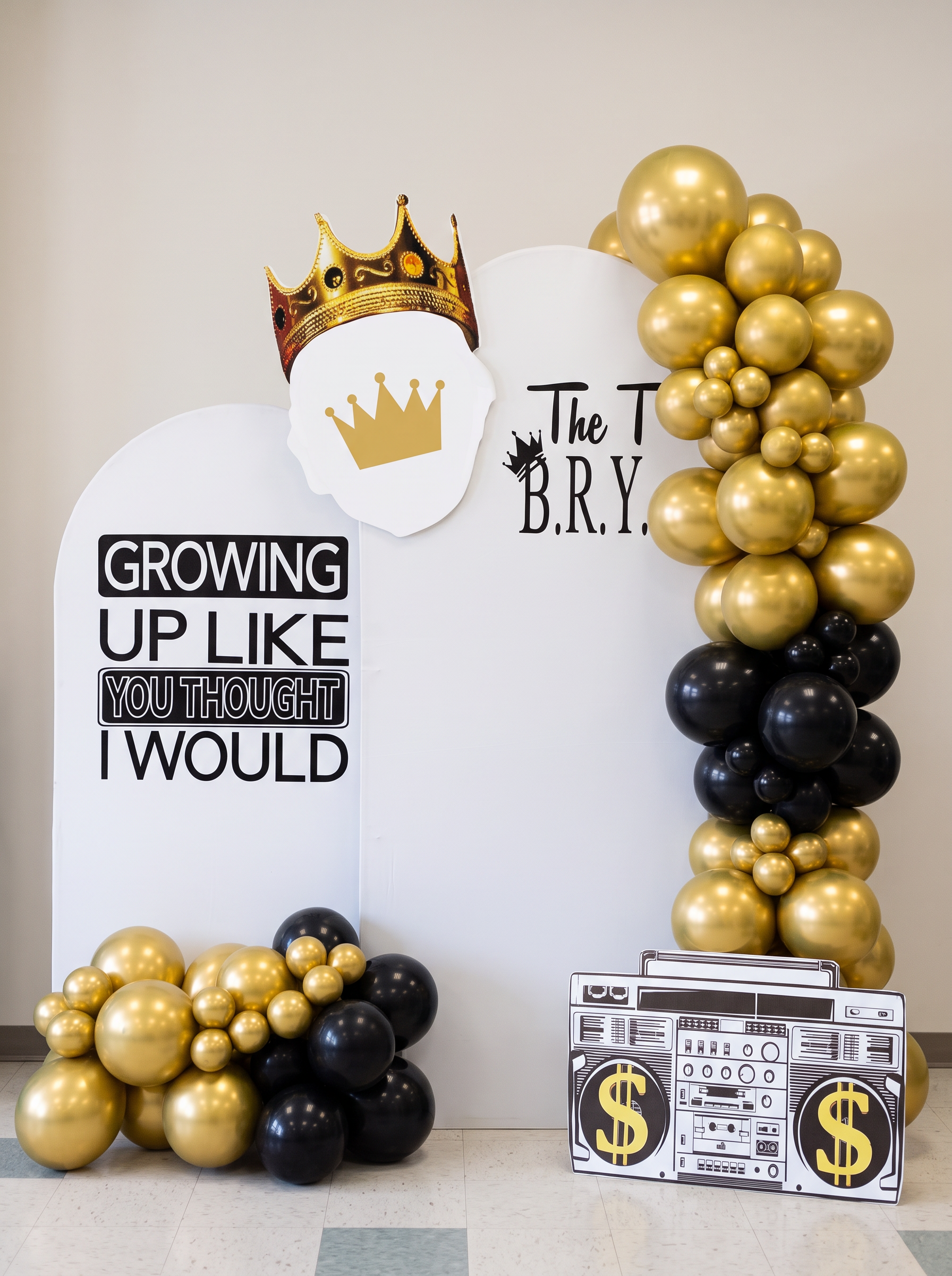 First birthday backdrop with gold and black balloon garland, lettering panels, crown cutout and a boombox cutout