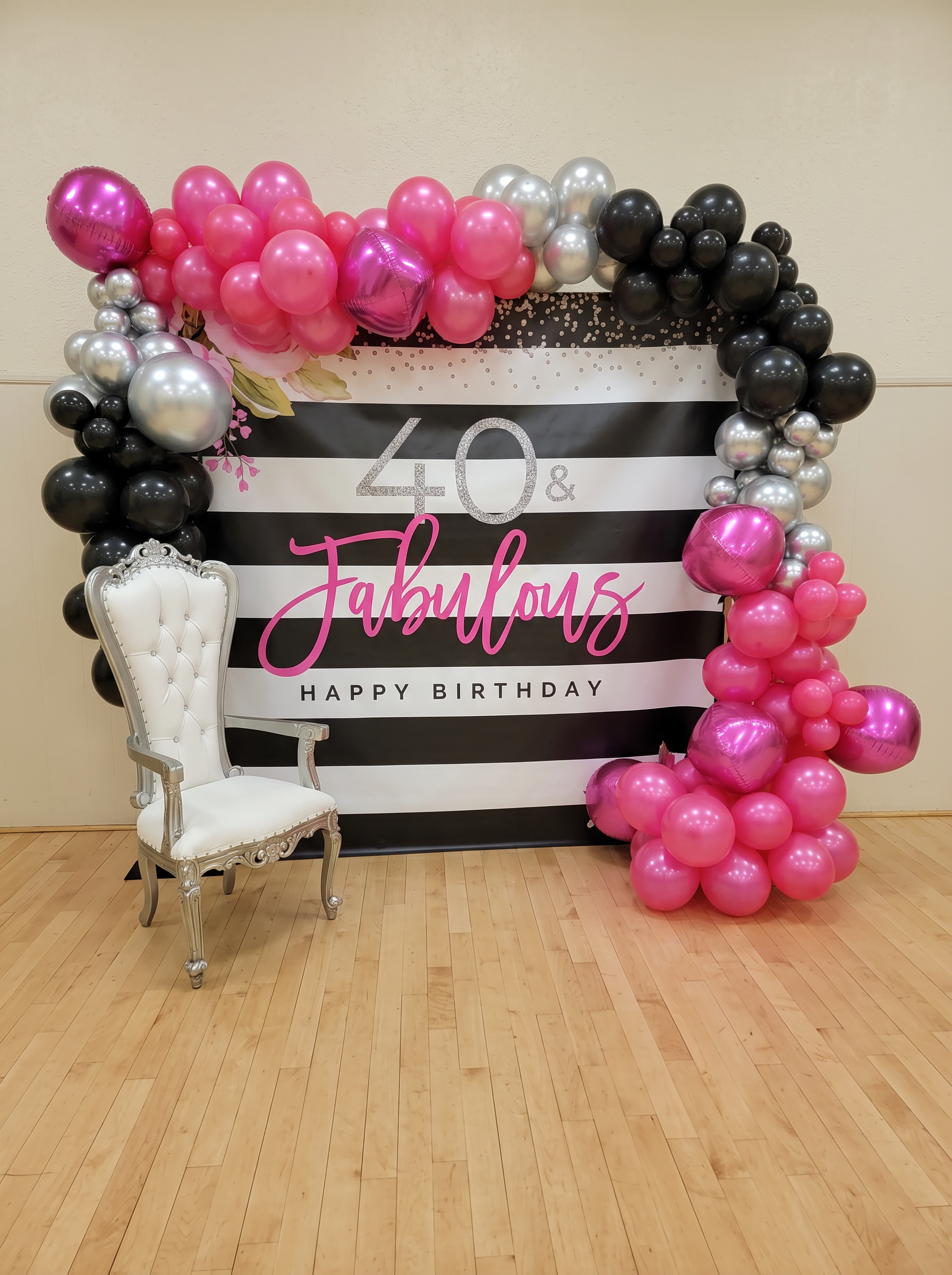 40 and Fabulous black and white striped birthday backdrop framed by a hot pink, black and silver balloon garland