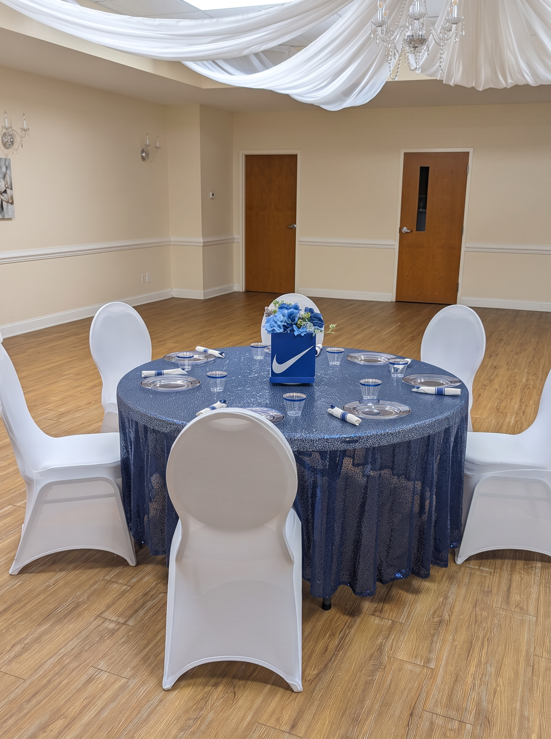 Guest table with a navy sequin linen, silver-rimmed plates and a blue floral box centerpiece