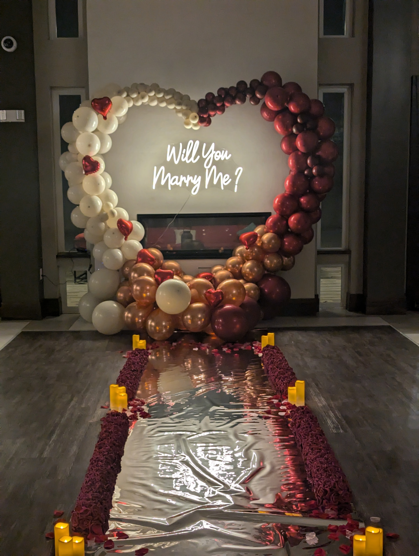 Proposal heart balloon arch with a Will You Marry Me neon sign, petal aisle and candles
