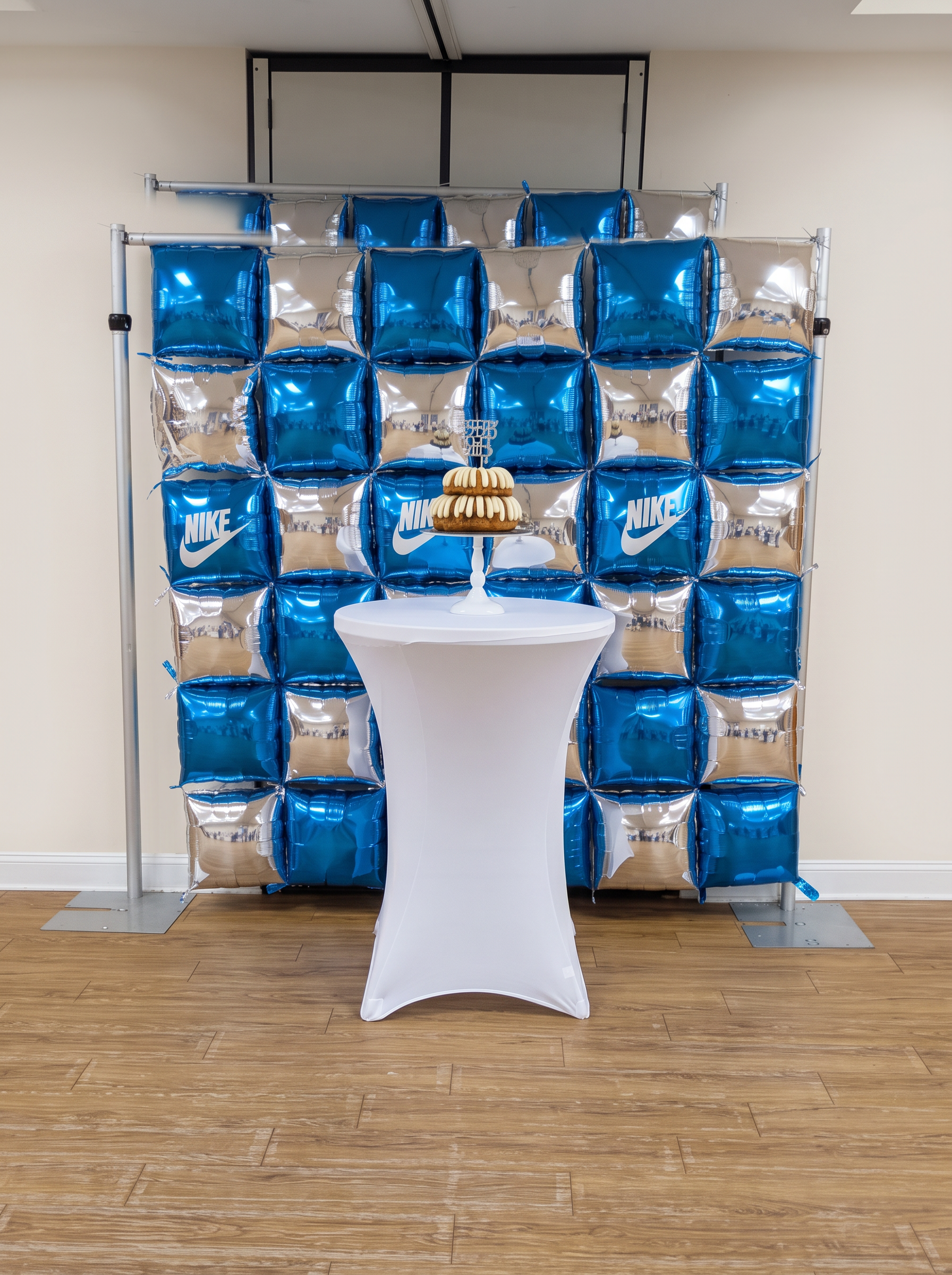 Blue and silver foil pillow balloon wall behind a white cocktail table holding a tiered cake