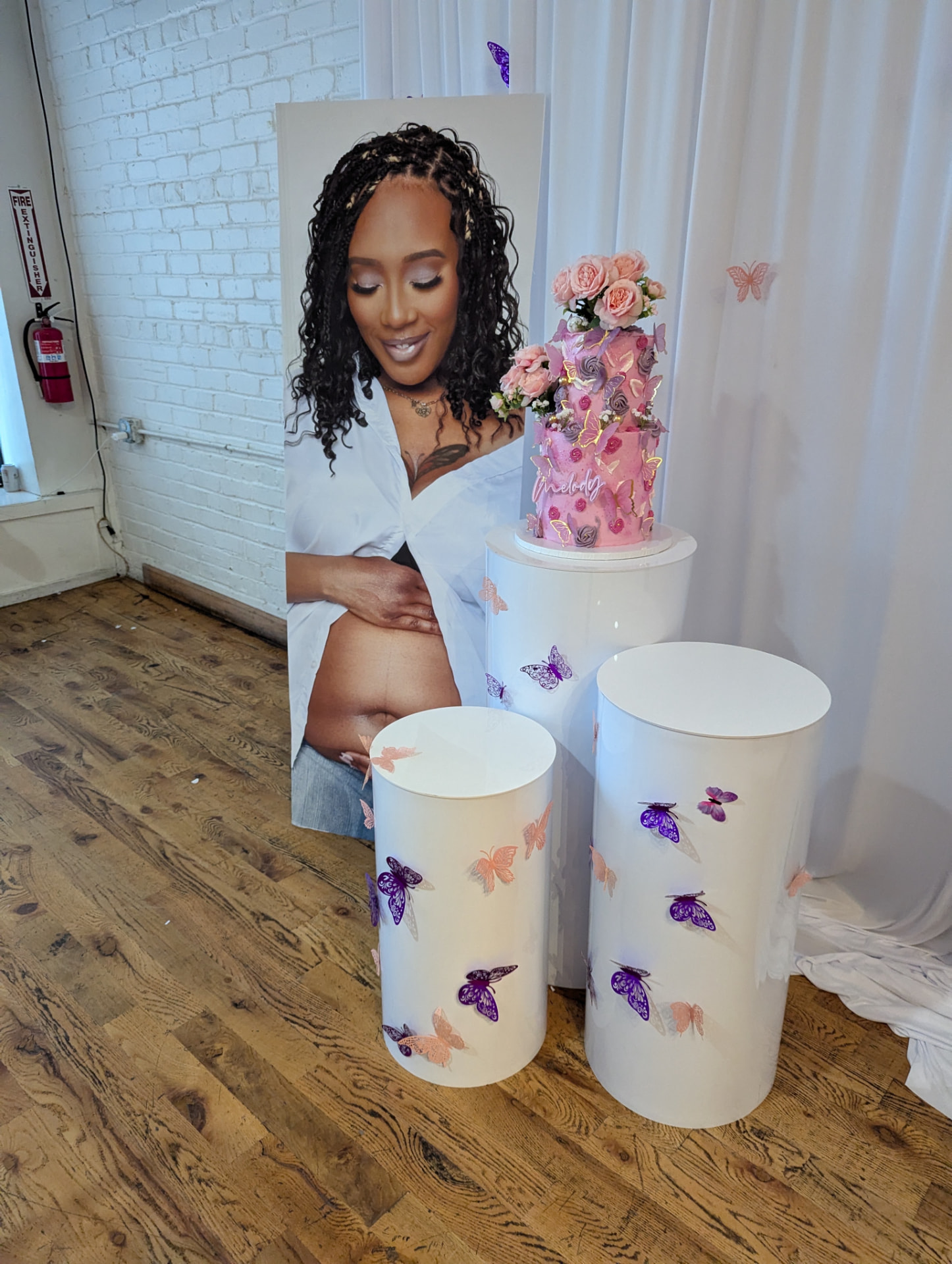 Baby shower butterfly cylinder plinths beside a life-size photo cutout of the mom-to-be