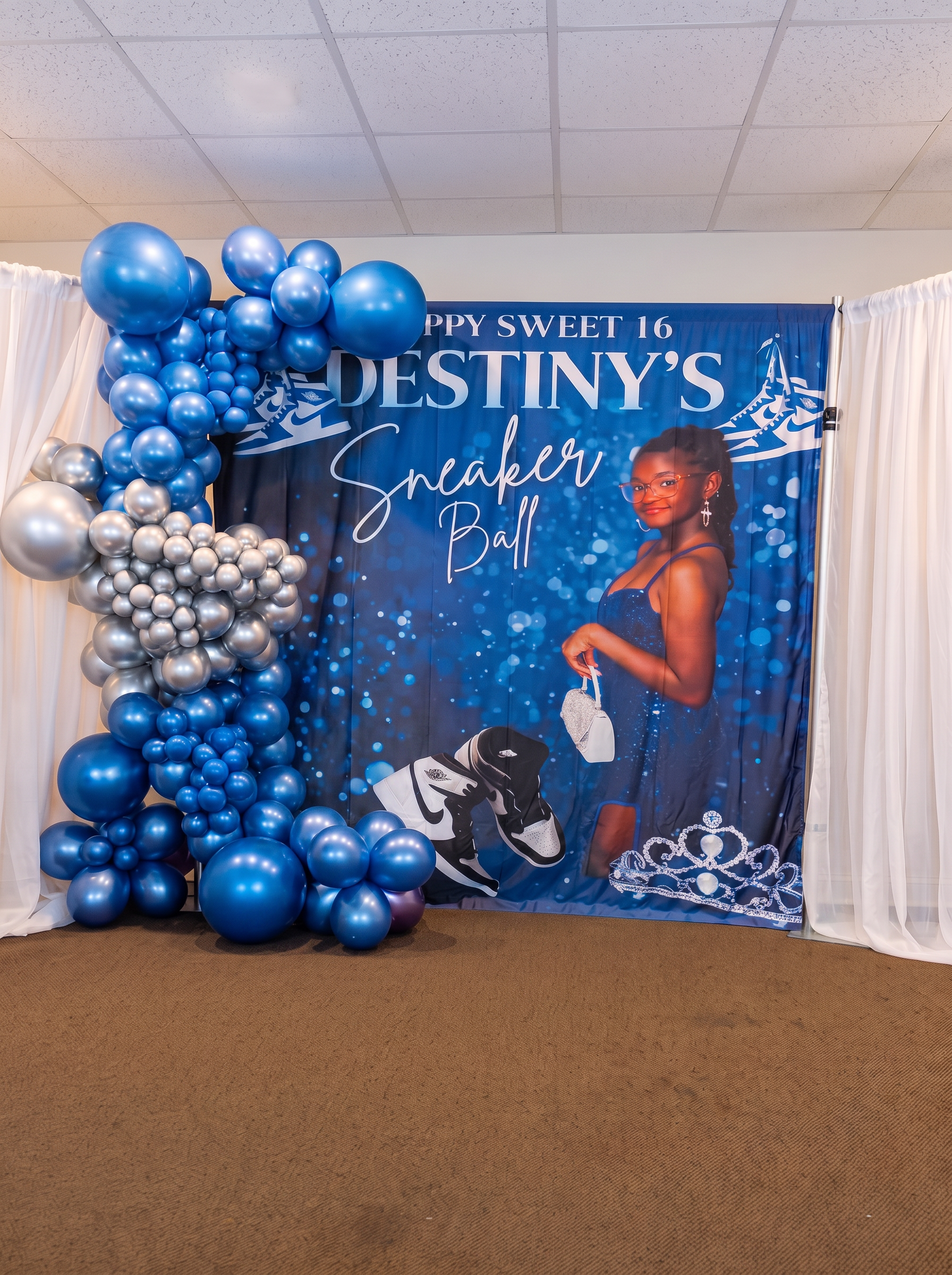 Sweet sixteen sneaker ball backdrop with a blue and silver chrome balloon garland and white draping